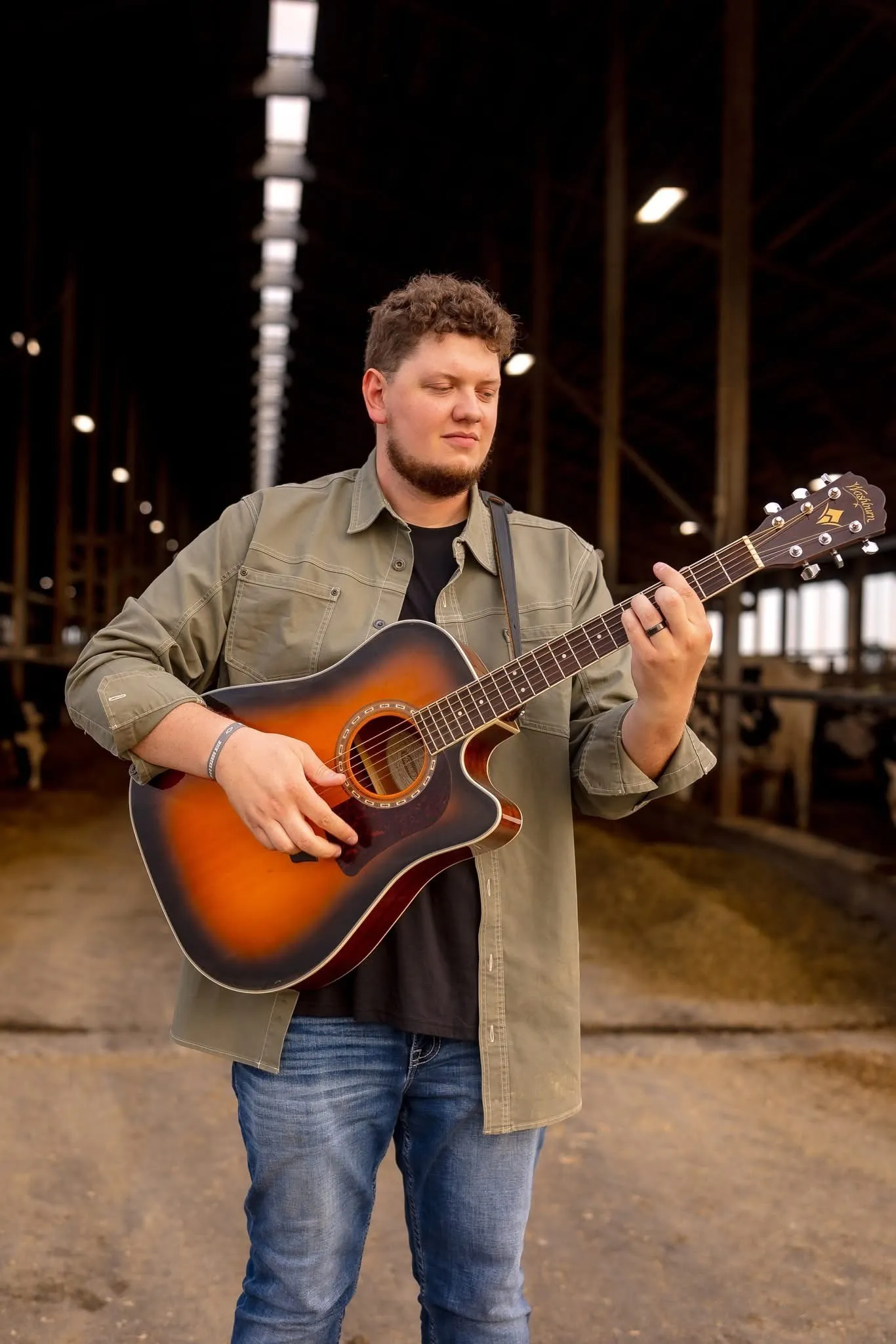 Isaac Buschur playing acoustic guitar inside a dairy barn