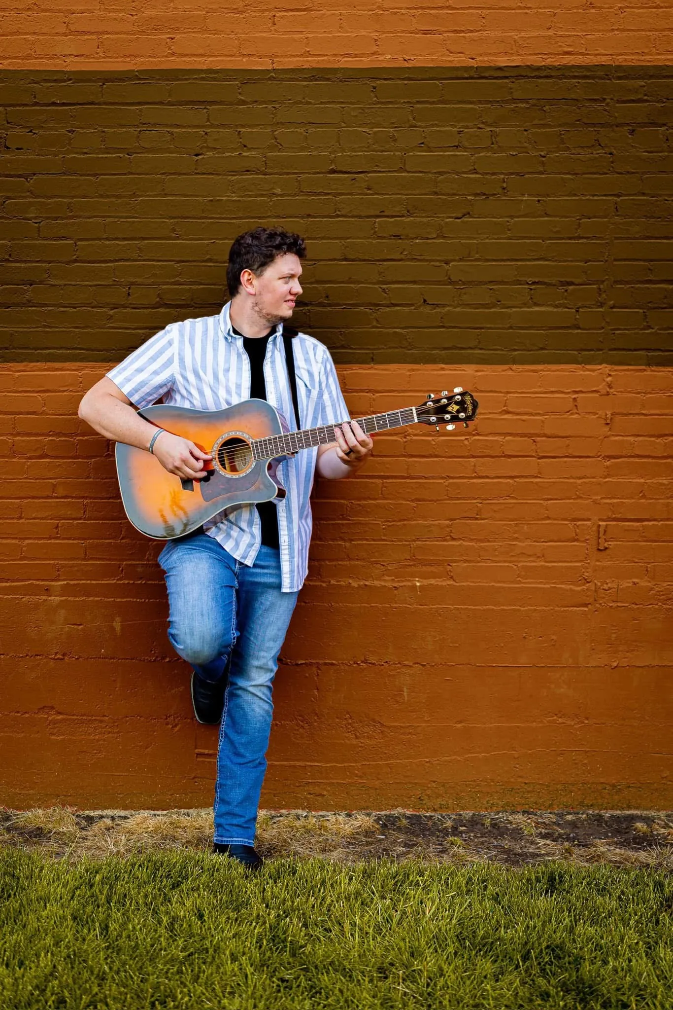 Isaac Buschur leaning on a painted brick wall with his guitar